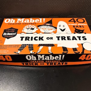 May include: An orange and white rectangular box of Oh Mabel! toasted coconut candy bars. The box features illustrations of children in Halloween costumes, a black cat, and the text Trick or Treats. It contains 40 wrapped miniature bars, net weight 1 lb. 2 oz.