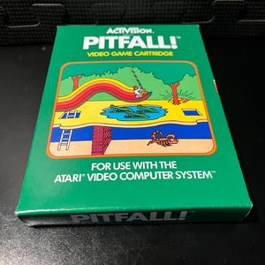 May include: Green Pitfall! video game cartridge for the Atari Video Computer System. The box features a colorful illustration of a jungle scene with a swinging figure, crocodiles, and a scorpion. The Activision logo is at the top.