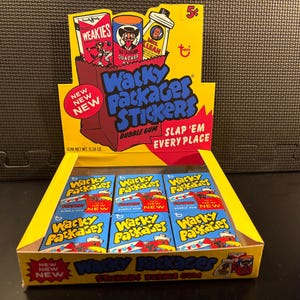 May include: A display box of Wacky Packages Stickers bubble gum. The box is yellow and red with the text "Wacky Packages Stickers" in blue. The box contains several packs of gum with the same design. The display also has a "New" sticker.