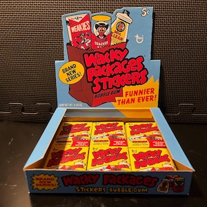 May include: A display box of vintage Wacky Packages Stickers bubble gum. The box is blue and yellow, with the words "Wacky Packages Stickers Bubble Gum" in red and white. The display includes individual packs of stickers and a header with cartoon illustrations.