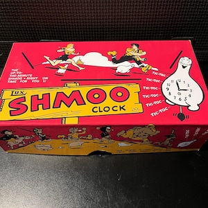 May include: A vintage red box featuring a cartoon illustration of people and a clock. The box reads "Lux Shmoo Clock" in yellow lettering. The clock face is white with black numbers and hands, and the pendulum reads "Tic-Toc".
