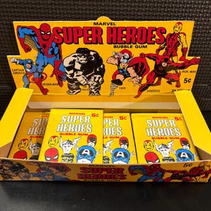 May include: A yellow cardboard display box of Marvel Super Heroes bubble gum. The box features illustrations of Spider-Man, Captain America, Hulk, Thor, Daredevil, and Iron Man. Each gum pack is 5 cents.