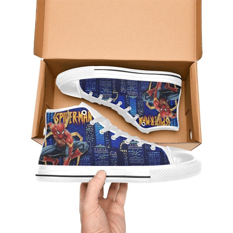 Op de afbeelding: Paar hoge canvas sneakers met een Spider-Man-ontwerp. De schoenen hebben een blauwe stadsgezicht achtergrond met Spider-Man graphics. De sneakers zijn wit met blauwe en rode accenten en zitten in een kartonnen doos.