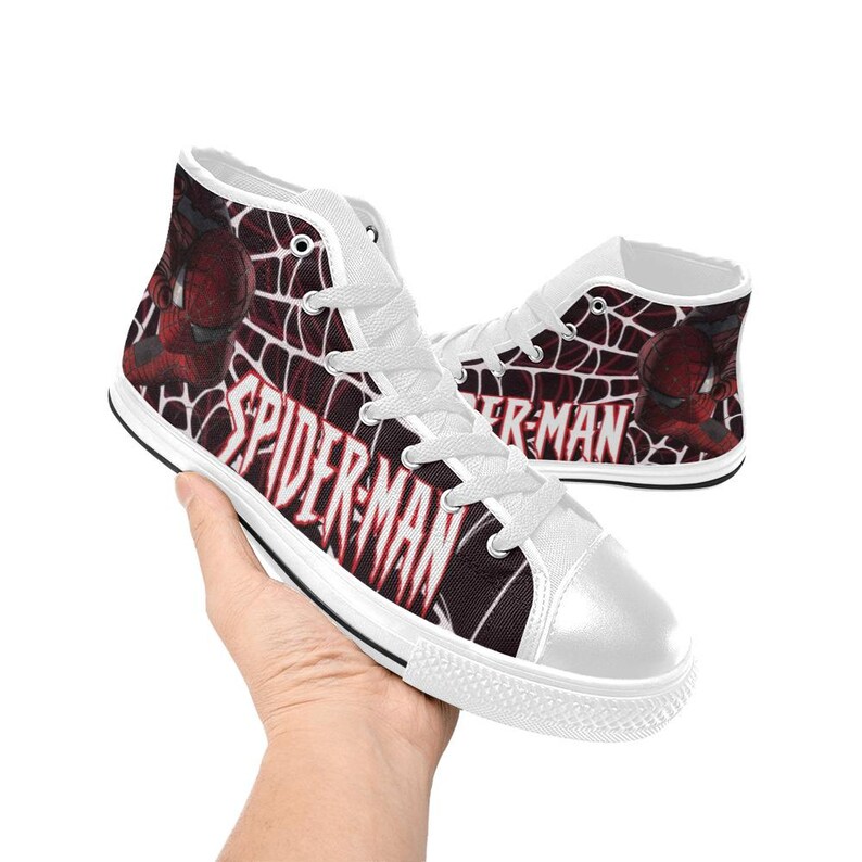 May include: High-top canvas sneakers featuring a Spider-Man design. The shoes have a white toe cap and laces, with the words "SPIDER-MAN" in red and white. The sides display a web pattern and a Spider-Man graphic.