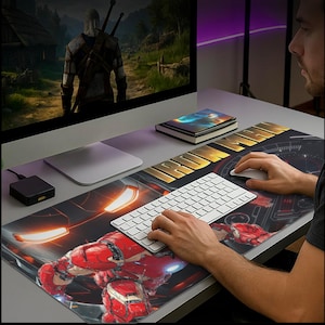 Könnte beinhalten: Ein großes rechteckiges Mauspad mit einem rot-goldenen Iron Man-Design. Die Worte "IRON MAN" sind in Gold gedruckt. Eine weiße Tastatur und Maus befinden sich auf dem Pad. Ein Computermonitor zeigt ein Videospiel.