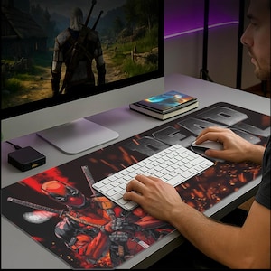 May include: A large rectangular mouse pad featuring a Deadpool graphic in red and black. The pad also has the word "DEAD" in large, gray letters. A white keyboard and mouse are on the pad.