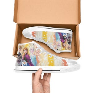 May include: White high-top sneakers featuring a colorful design with characters from the animated movie. The shoes have a white rubber sole and laces. The design includes images of Elsa, Anna, Olaf, and other characters.