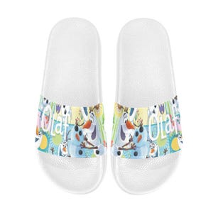 Puede incluir: Un par de sandalias deslizantes blancas con una banda colorida con el personaje Olaf de Frozen. La banda tiene un fondo azul, amarillo y verde con la palabra "Olaf" e im&aacute;genes de Olaf.