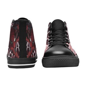 May include: High-top sneakers with a black rubber sole and black laces. The sneakers feature a red and white pattern on the sides and a red and black design on the back. The shoes have a black toe cap and a white stripe on the sole.