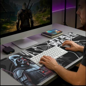 Könnte beinhalten: Eine schwarz-weiße Star Wars-Schreibtischunterlage mit Darth Vader. Die Matte hat eine große Grafik von Darth Vader in der unteren linken Ecke. Eine weiße Tastatur und Maus befinden sich auf der Matte. Ein Computermonitor befindet sich im Hintergrund.