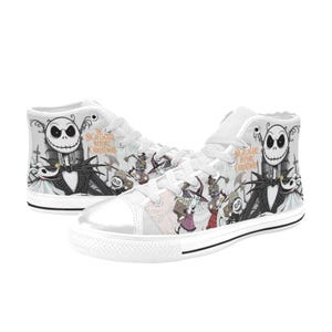 Puede incluir: Zapatillas altas blancas con personajes de "Pesadilla antes de Navidad". Los zapatos muestran a Jack Skellington y otros personajes en un dise&ntilde;o gris y negro. Tambi&eacute;n es visible el texto "The Nightmare Before Christmas".