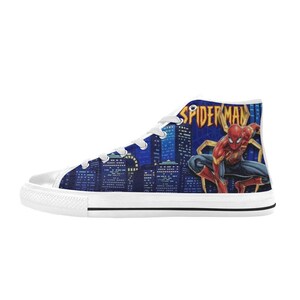 Op de afbeelding: Hoge canvas sneakers met een blauw stadslandschapontwerp met het Spider-Man-logo en -personage. De schoenen hebben witte veters, een witte rubberen neus en een witte zool.