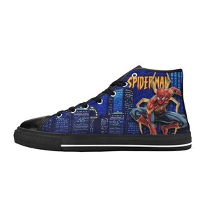 Op de afbeelding: Hoge canvas sneaker met een Spiderman-afbeelding. De schoen heeft een zwarte neus en zool, met een blauwe skyline-achtergrond. Het Spiderman-logo is zichtbaar aan de zijkant.