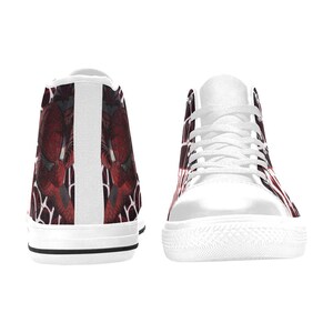 May include: White high-top sneakers with a red and black graphic design. The sneakers have white laces, a white sole, and a black stripe along the bottom. The design appears on the sides and back of the shoes.