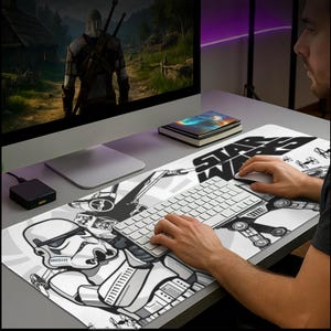 May include: A Star Wars themed desk mat featuring a black and white design with a Stormtrooper, AT-AT, and the Star Wars logo. The mat is rectangular and covers the desk surface, with a keyboard and mouse on top.