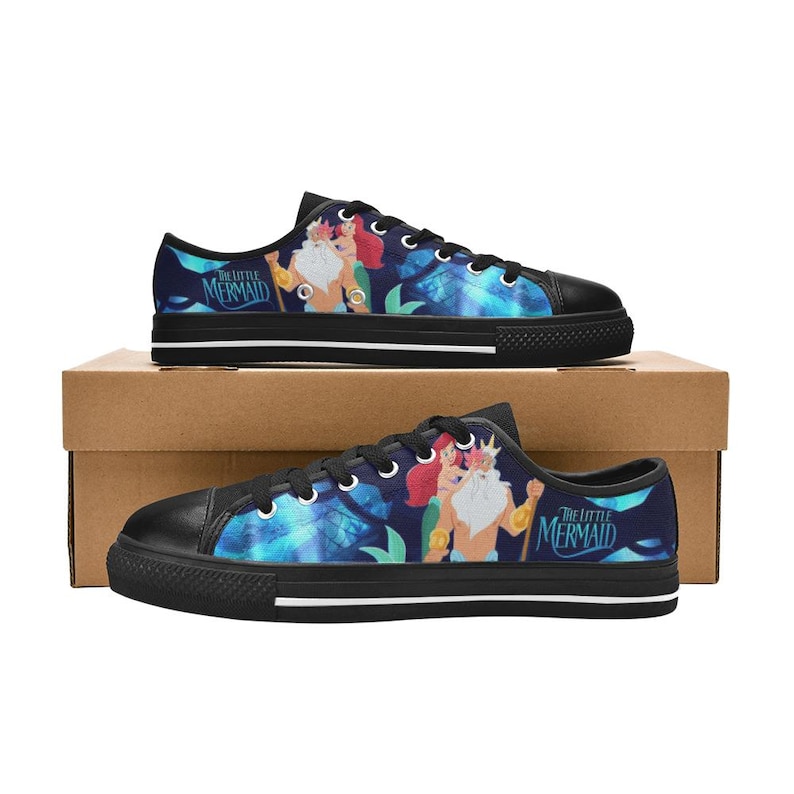 May include: Pair of black-soled canvas sneakers featuring a colorful design from "The Little Mermaid." The shoes display Ariel, King Triton, and a blue and teal underwater scene. The text "The Little Mermaid" is visible.