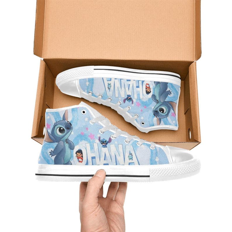 Puede incluir: Zapatillas altas de lona con un dise&ntilde;o azul y blanco con la palabra "OHANA" y un personaje de dibujos animados. Las zapatillas est&aacute;n en una caja de cart&oacute;n, con una zapatilla visible y la otra parcialmente visible.