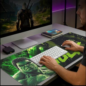 Könnte beinhalten: Rechteckige grüne und schwarze Mausunterlage mit Hulk-Motiv. Das Gesicht von Hulk ist auf der linken Seite zu sehen. Eine weiße Tastatur und Maus befinden sich auf der Unterlage. Ein Computermonitor ist sichtbar.
