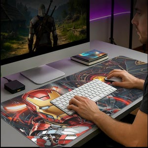 May include: A large rectangular mouse pad featuring a vibrant Iron Man design in red, gold, and black. The pad is placed on a desk with a white keyboard, mouse, and computer monitor displaying a video game scene.