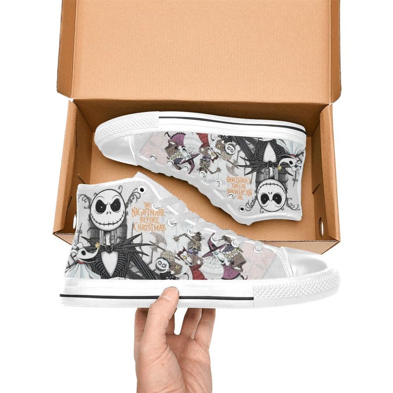 Puede incluir: Zapatillas altas blancas con personajes e im&aacute;genes de "Pesadilla antes de Navidad". Los zapatos tienen un dise&ntilde;o en blanco y negro con el texto "The Nightmare Before Christmas" en el lateral. Las zapatillas est&aacute;n en una caja de cart&oacute;n abierta.