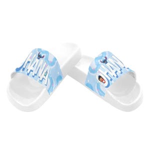 Puede incluir: Sandalias deslizantes blancas con un dise&ntilde;o azul y blanco con la palabra "OHANA" y personajes de dibujos animados. Las sandalias tienen una suela plana y est&aacute;n dise&ntilde;adas para uso casual.