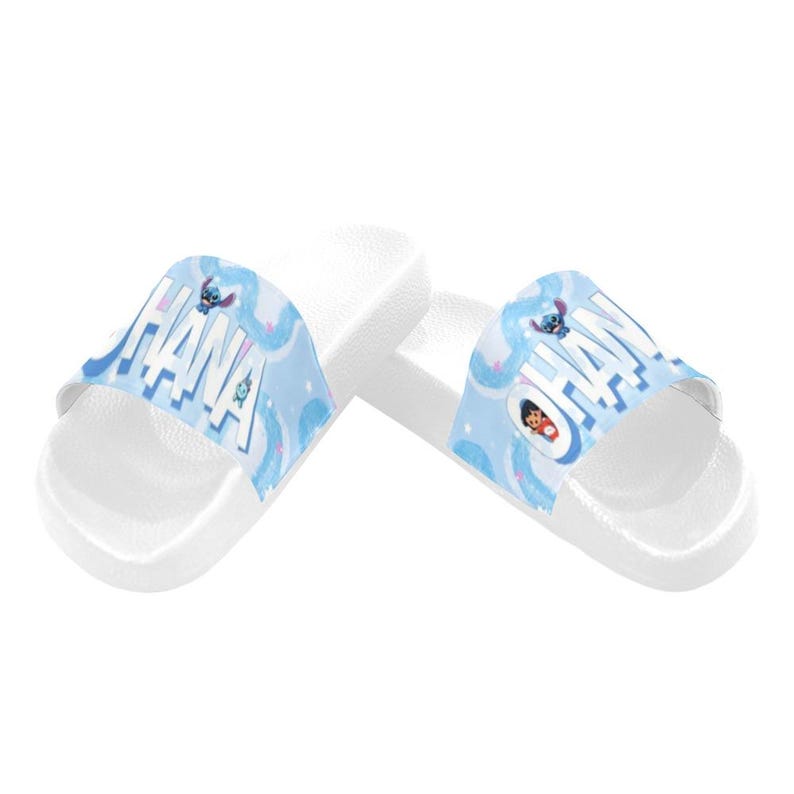 Puede incluir: Sandalias deslizantes blancas con un dise&ntilde;o azul y blanco con la palabra "OHANA" y personajes de dibujos animados. Las sandalias tienen una suela plana y est&aacute;n dise&ntilde;adas para uso casual.