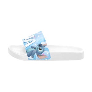 Puede incluir: Sandalia deslizante blanca con un gr&aacute;fico azul y blanco del personaje Stitch de la pel&iacute;cula Lilo & Stitch. La sandalia tiene una correa azul con la palabra "Lilo" y una imagen de dibujos animados de Stitch.