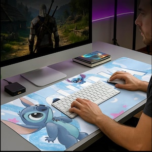 Pode incluir: Um tapete de mesa azul e branco com o tema Stitch, com o personagem Stitch de Lilo & Stitch. O tapete tem um fundo azul claro com nuvens e estrelas brancas. Um teclado e um rato brancos estão em cima.