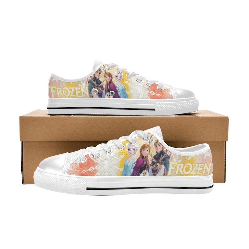 Puede incluir: Zapatillas de lona blancas con un dise&ntilde;o colorido con personajes de la pel&iacute;cula "Frozen". Los zapatos tienen cordones blancos, una suela de goma blanca y la palabra "FROZEN" impresa en el lateral.