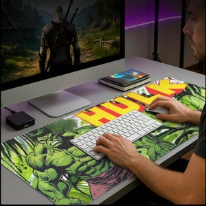 May include: A green and purple Hulk-themed mousepad with the word "HULK" in yellow and red. The mousepad features a graphic of the Hulk and is placed on a gray desk with a computer, keyboard, and mouse.