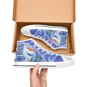 Puede incluir: Zapatillas altas de lona con una imagen de dibujos animados de Olaf de Frozen. Los zapatos tienen suela y cordones de goma blancos, con un fondo azul y morado. La palabra "Olaf" est&aacute; impresa en el lateral.