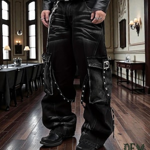 May include: Black denim cargo pants with multiple pockets, straps, and silver hardware. The pants have a distressed wash and a wide leg fit. The model is wearing a black leather jacket and black shoes. The pants have a chain detail.