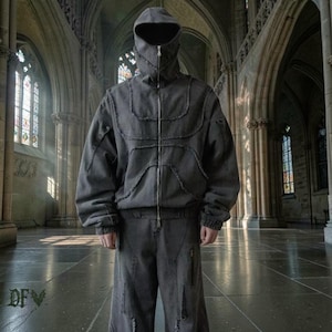 Puede incluir: Conjunto de chaqueta con capucha y pantalón gris oscuro. La chaqueta presenta una cremallera completa, paneles cosidos únicos y una capucha que cubre toda la cabeza. Los pantalones tienen un corte holgado con bolsillos con cremallera. El conjunto es una versión moderna del streetwear.
