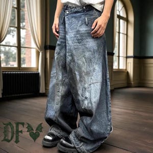 Może przedstawiać: Szerokie dżinsy z efektem sprania i unikalnym designem w stylu kopertowym. Spodnie mają zapięcie na guziki, kieszenie i szeroką nogawkę. Model nosi czarne buty. Obraz zawiera również litery "DF" z sercem i wzorem skrzydła.