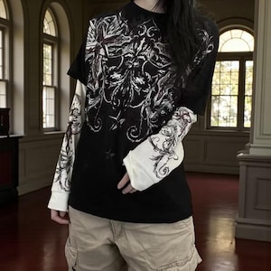 以下が含まれることがあります： 黒い半袖Tシャツと、その下に白い長袖シャツ。 黒いシャツは白と赤の装飾的なデザインが特徴です。 白い袖にも同様のデザインが施されています。 カーキ色のカーゴショーツを着用しています。