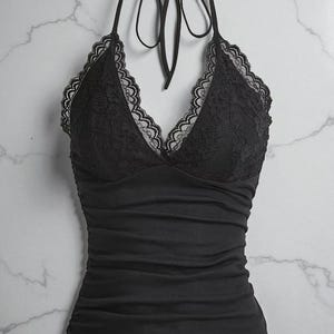 May include: Black halter top with a lace bodice and a gathered, fitted bottom. The top features a tie closure at the neck and a scalloped lace trim. The fabric appears to be a soft, stretchy material.