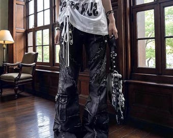 May include: Black denim pants with distressed details, cargo pockets, and a flared leg. The pants have a raw hem and are paired with platform shoes. A white t-shirt with graphic text is visible.