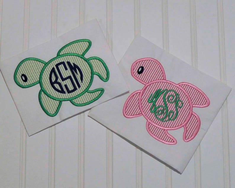 May include: Two embroidered sea turtle designs on white fabric. One turtle is green with a monogram in the center, and the other is pink with a green swirl design.