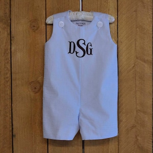 May include: A light blue and white striped baby overall with a brown monogram "DSG" on the front.