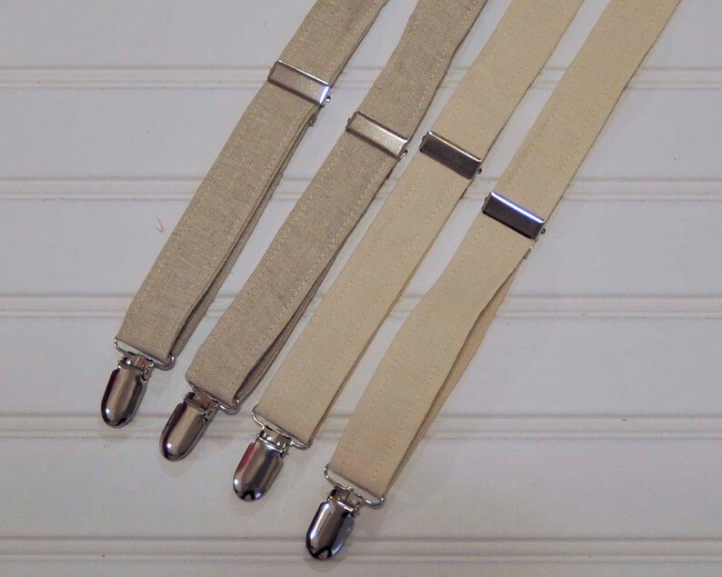 May include: Three pairs of beige suspenders with silver metal clips. The suspenders are made of a woven fabric.
