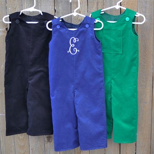 May include: Three pairs of corduroy overalls for children, one black, one blue with a white embroidered letter "E", and one green.