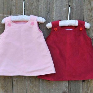 May include: Two sleeveless dresses hanging on hangers. The dress on the left is pink and the dress on the right is red.