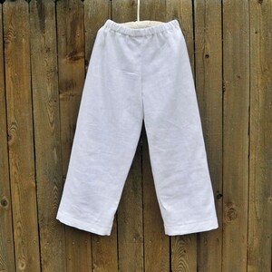 May include: White linen pants hanging on a wooden fence. The pants have a wide leg and a simple design.