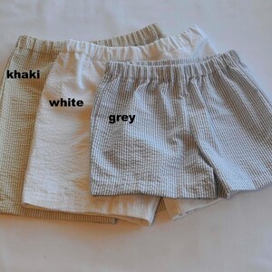 May include: Three pairs of shorts in khaki, white, and grey. The shorts are made of a lightweight fabric with a subtle texture. The shorts have a relaxed fit and are perfect for warm weather.