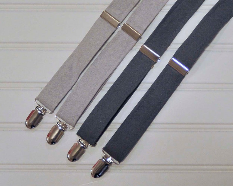 May include: Three pairs of suspenders, one pair is gray, one pair is light gray, and one pair is dark gray. The suspenders have silver metal clips.