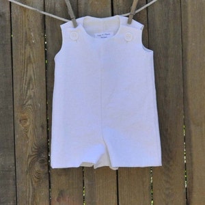 May include: A white sleeveless romper with button closures on the shoulders. The romper has a simple design and is made of a lightweight fabric.