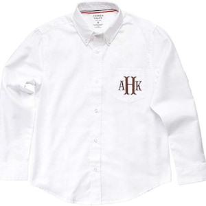 May include: White long-sleeve button-down shirt with a chest pocket. The pocket has a brown embroidered monogram "AHK" on it. The shirt has a label that says "French Toast" and "12".