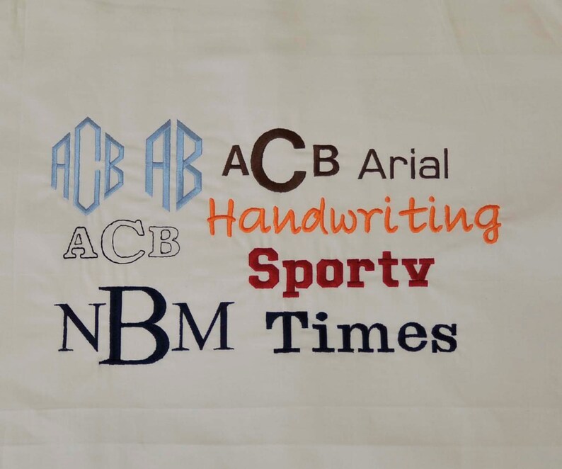 May include: A white fabric swatch with different embroidery styles of the letters "ACB" and "NBM". The styles include a monogram, block letters, handwriting, sporty, Arial, and Times New Roman fonts.