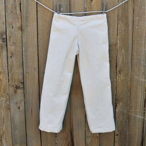 May include: White striped pants hanging on a wooden fence. The pants have a straight leg and a relaxed fit.