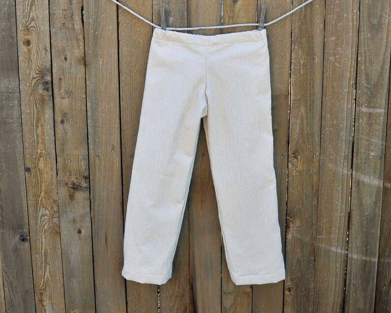 May include: White striped pants hanging on a wooden fence. The pants have a straight leg and a relaxed fit.